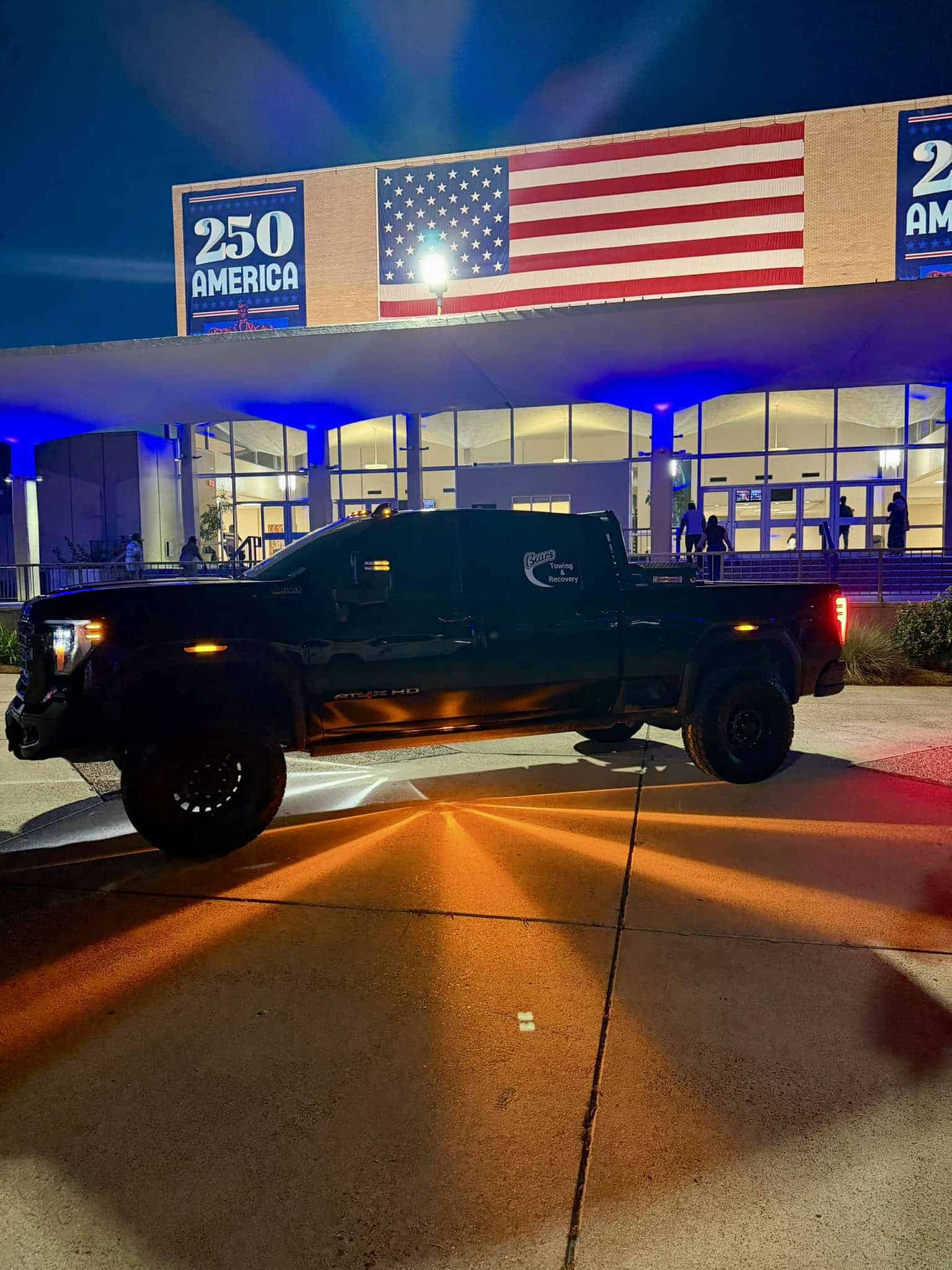 Black customer pickup with amber and white light patterns on the pavement outside an illuminated building.