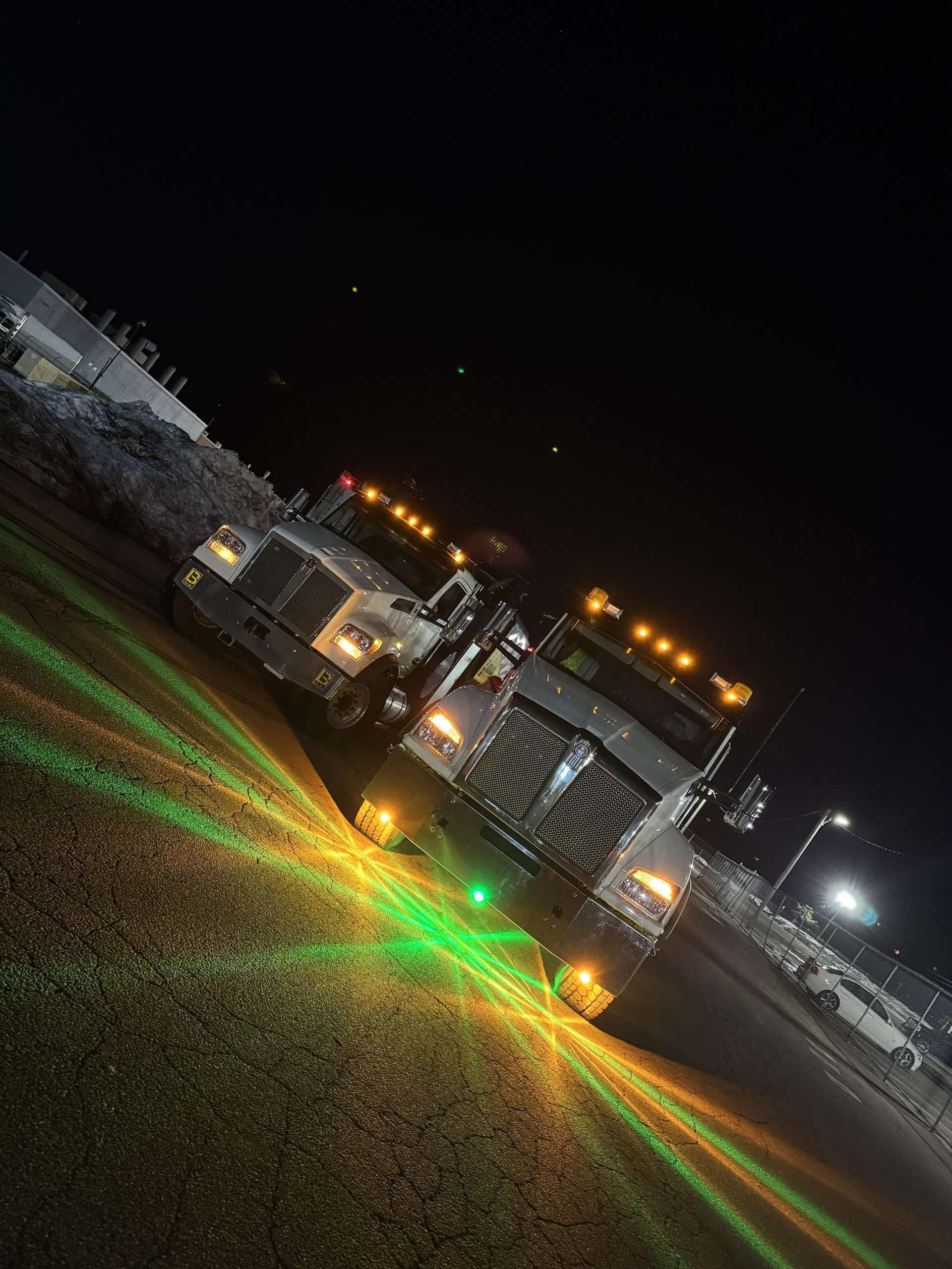 Two custom big rigs with green and amber Glass Is Class starburst light patterns beneath them